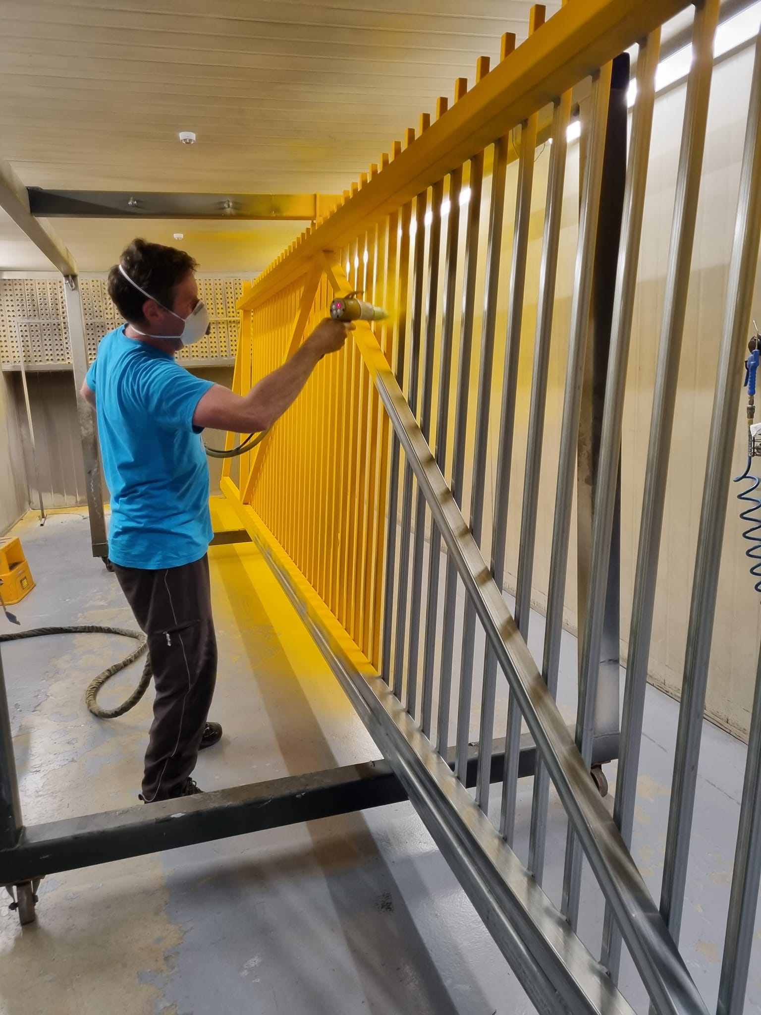 Person spray painting a metal railing yellow in an indoor setting.