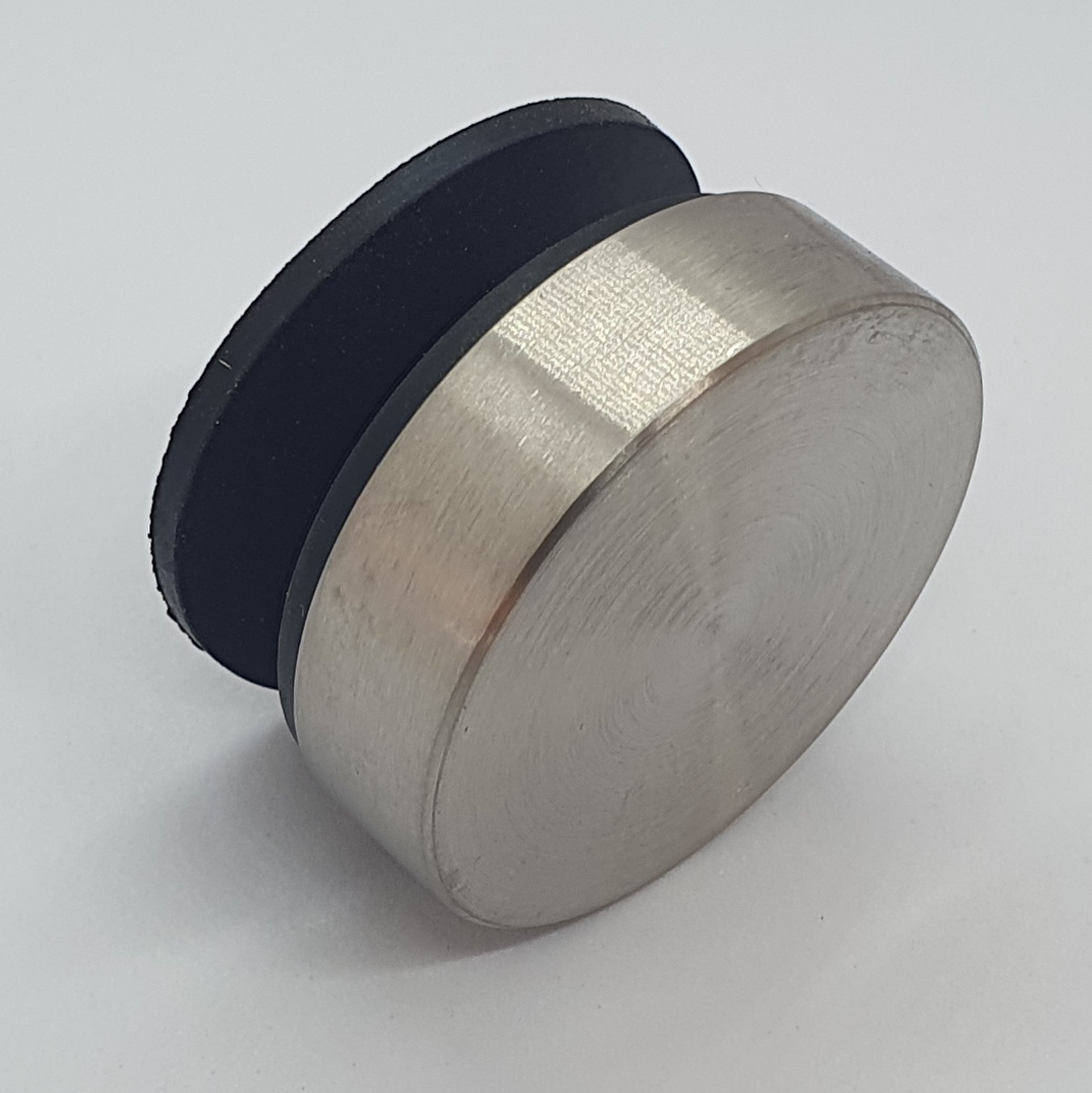 Round metallic object with black rubberized top on a light gray background